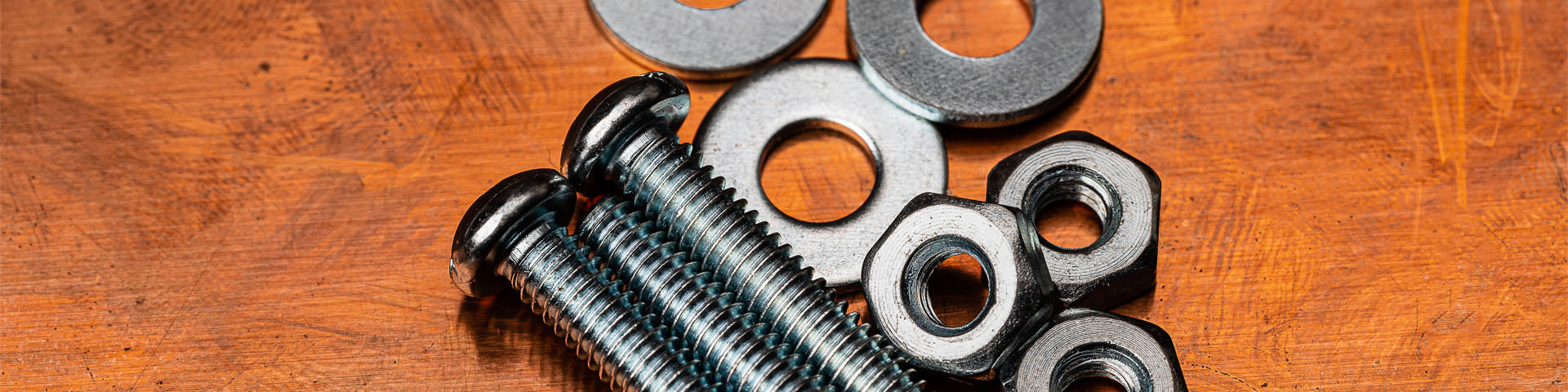 A Macro shot of several small stainless steel bolts, washers and nuts on a dirty and worn copper work surface. 