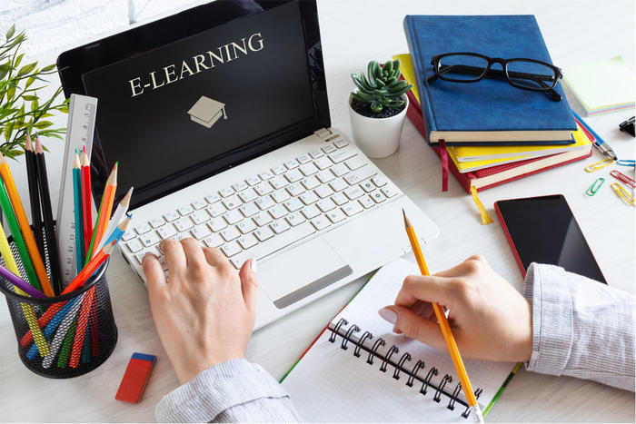 Person with pencil and paper with e-learning computer screen